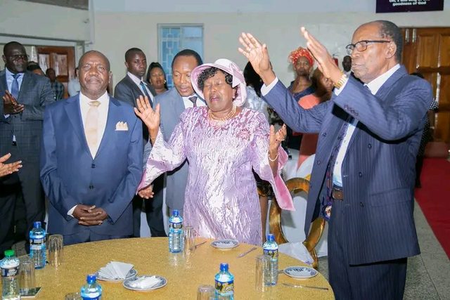 Three ministers with raised hands at a banquet table