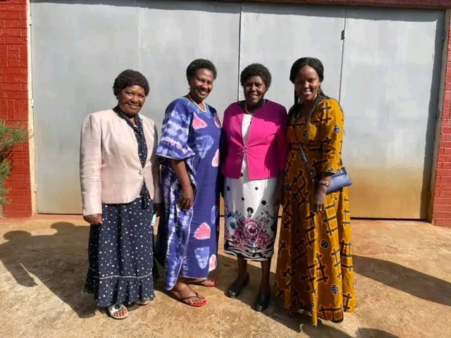 Four women standing together in front of a metal gate